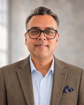 Rudy Agnihotri wearing glasses and a brown blazer